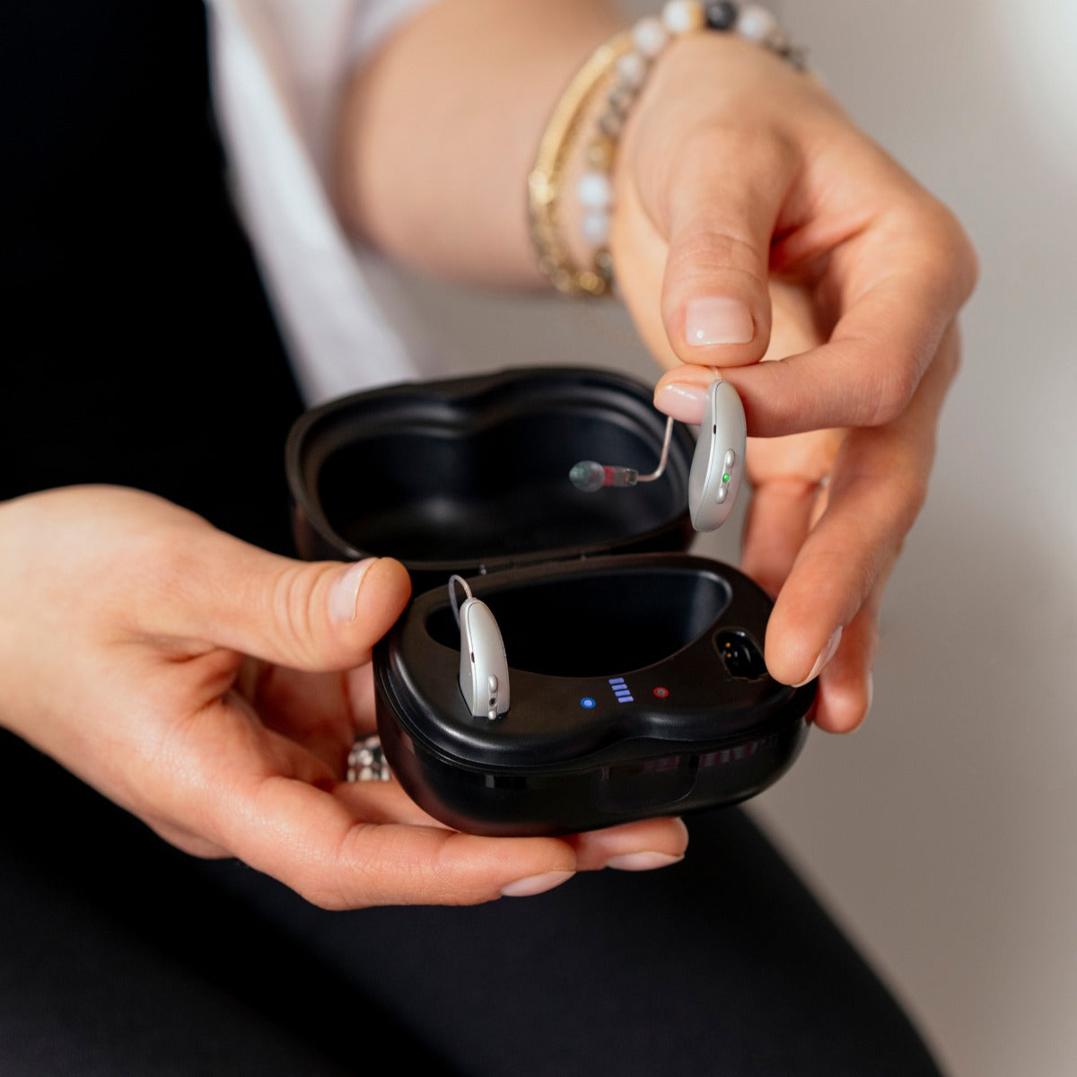 Lady's hands holding hearing aid charger and hearing aids 