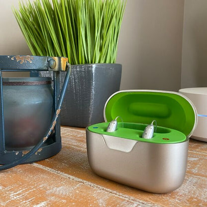 Charging case with neon green inside and hearing aids inserted sitting on wooden table 