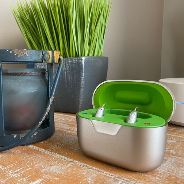 Charging case with neon green inside and hearing aids inserted sitting on wooden table 