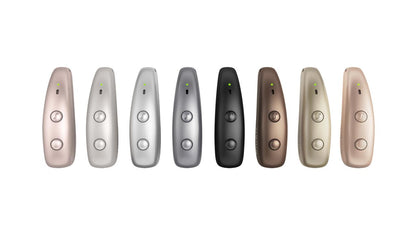 Seven sleek, metallic Signia Pure Charge&Go Max hearing aids in various colors (rose gold, silver grey, titanium grey, black, chestnut brown, honey blonde, beige, and dark champagne) arranged in a row against a solid white background.