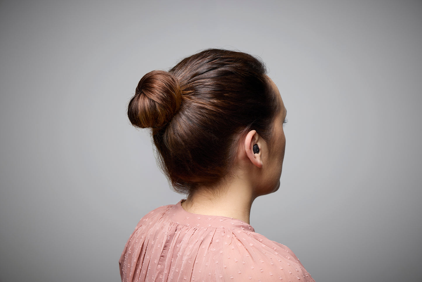 Person with a bun hairstyle on a gray background with hearing aid in her ear 