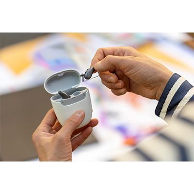Person inserting earbuds into a white charging case with a blurred colorful background